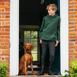 Person wearing a green hoodie standing next to a dog at a door.