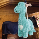 Plush dinosaur toy hanging from a strap with a horse in the background