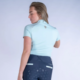 Woman wearing a light blue equestrian shirt and dark blue leggings on a white background