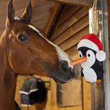Horse interacting with a penguin toy holding a carrot in a stable setting
