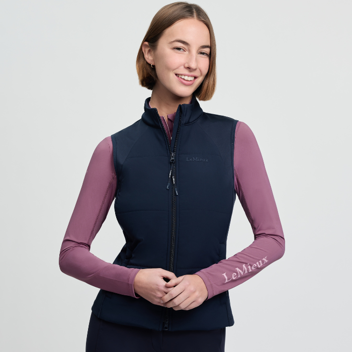 Woman wearing a navy gilet with pink base layer and 'LeMieux' branding on a light grey background
