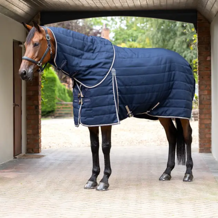 Horse wearing a blue quilted stable rug standing in a stable.