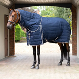 Horse wearing a blue quilted stable rug standing in a stable.