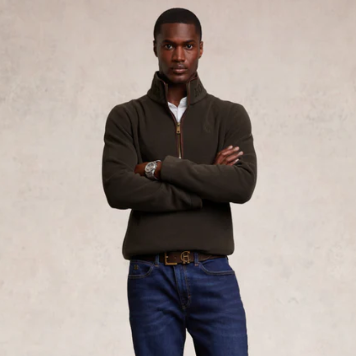 Man wearing a dark khaki sweater and blue jeans against a beige background