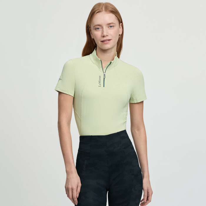 Woman wears a light yellow short sleeve base layer and dark leggings on a white background