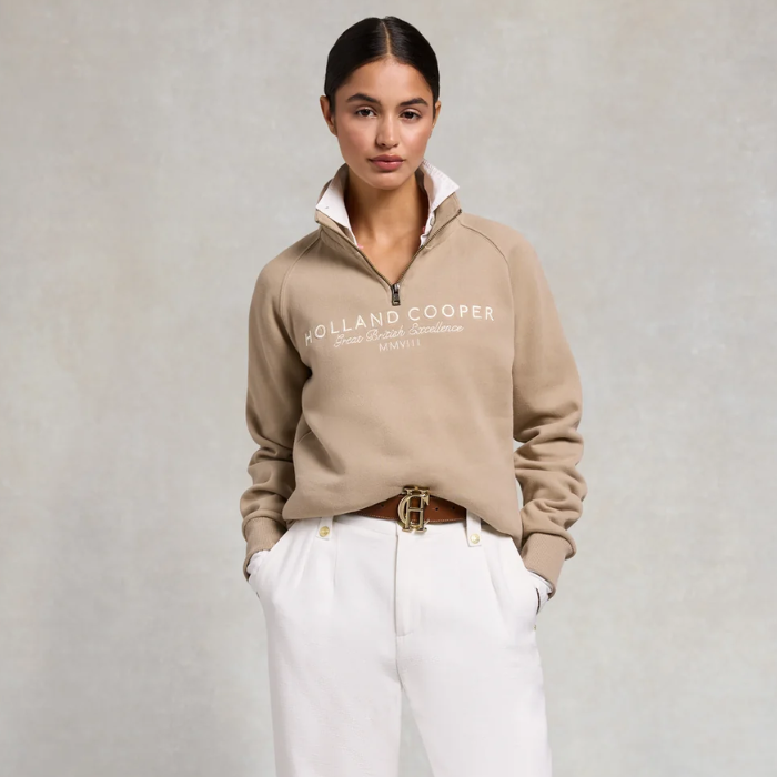 Woman wearing a beige sweatshirt and white trousers on a grey background