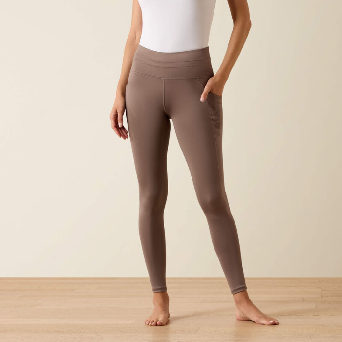 Person wears a pair of brown riding tights and a white top on a beige background