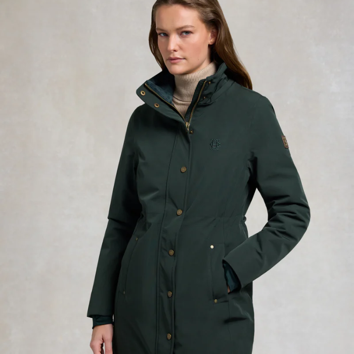 Woman wears a dark green rain coat on a plain background