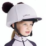 Child wearing a lilac equestrian helmet with black pom-poms and 'LeMieux' branding.