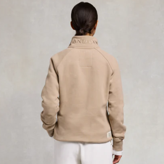 Person wearing a beige jacket with branding on a light grey background
