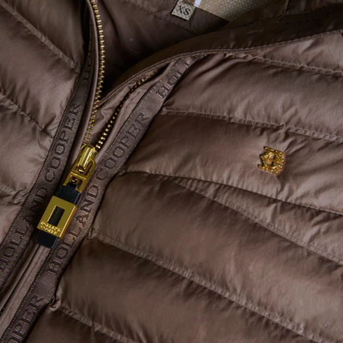 Close-up of a brown quilted jacket with gold zipper and logo, featuring the Holland Cooper brand.