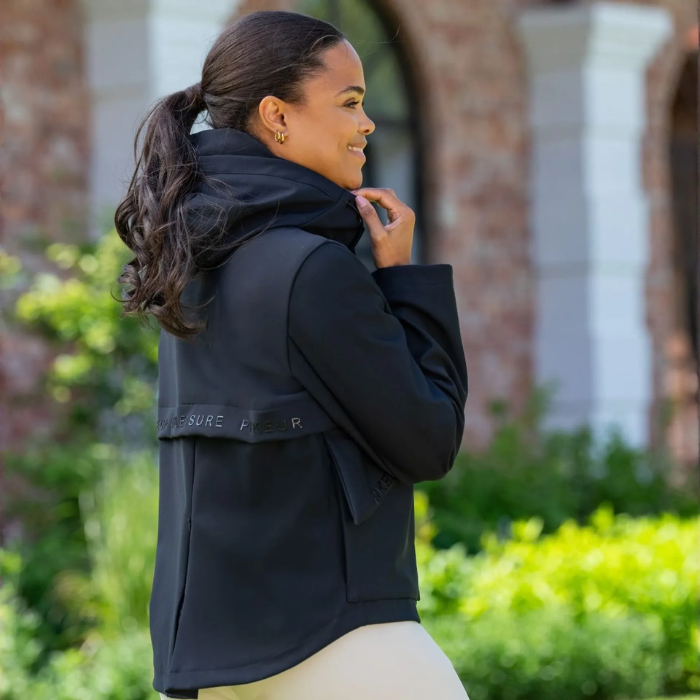 Woman wearing a black jacket outdoors with greenery in the background