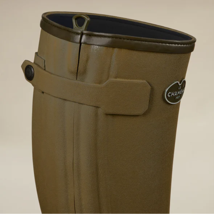 Close up of a green wellington boot with Le Chameau branding against a beige background