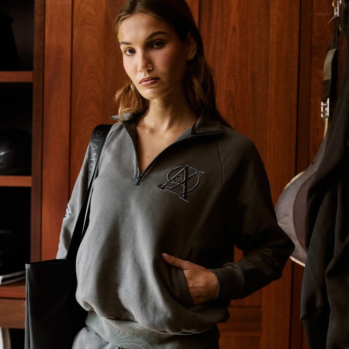 Woman wears a grey zipped sweatshirt against wood panelled wall