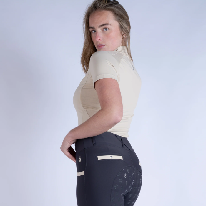 Woman wearing a beige top and dark leggings against a light grey background