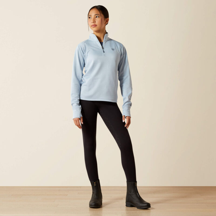 Woman wearing a light blue pullover, black leggings, and black boots on a beige background