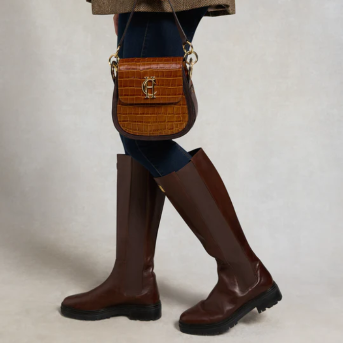 Brown knee-high boots and a brown handbag on a neutral background