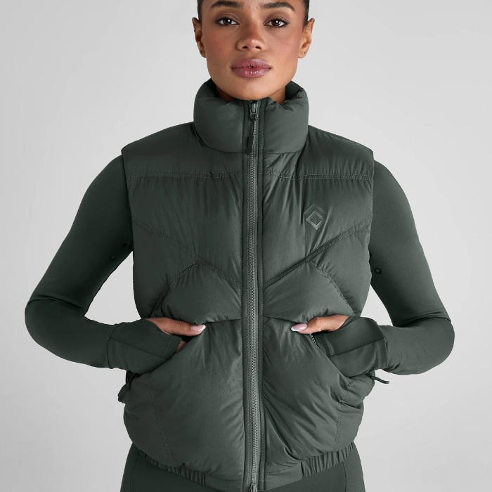 Woman wears a green gilet with brand logo on a grey background