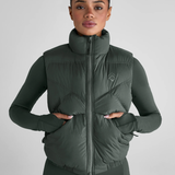 Woman wears a green gilet with brand logo on a grey background