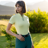 Woman wears a light yellow short sleeve base layer with LeMieux branding in an outdoor setting