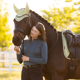 Woman stands with a brown horse against a blurred outdoor background