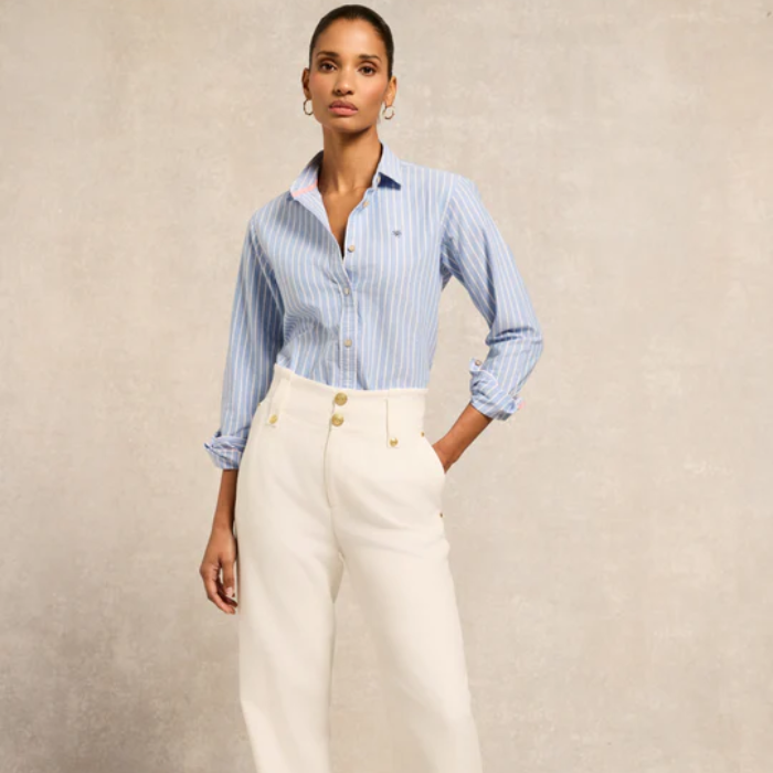 Woman wearing a blue striped shirt and white pants against a beige background
