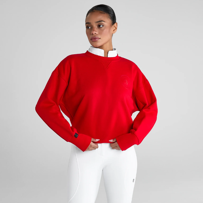 Woman wears a vibrant red sweater and white riding leggings on a grey background