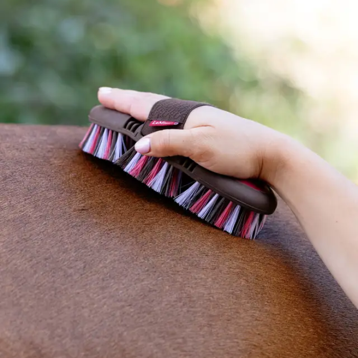 Red grooming brush being used on a horse's coat