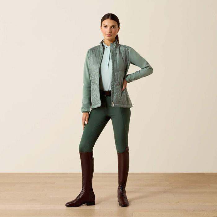 Woman wearing a green jacket, leggings, and brown boots on a beige background