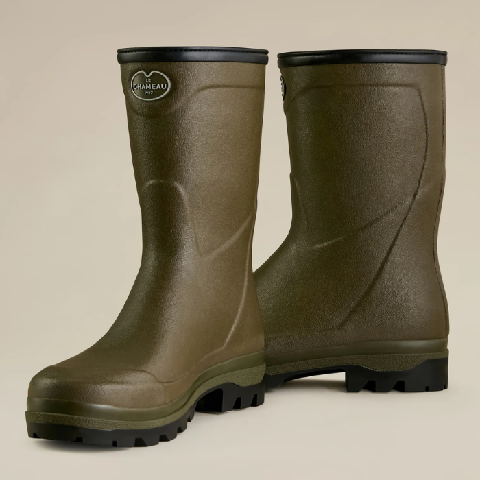 Pair of green rubber boots with black soles on a beige background