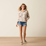 Woman wears a light beige sweatshirt with western pattern and denim shorts on a plain background