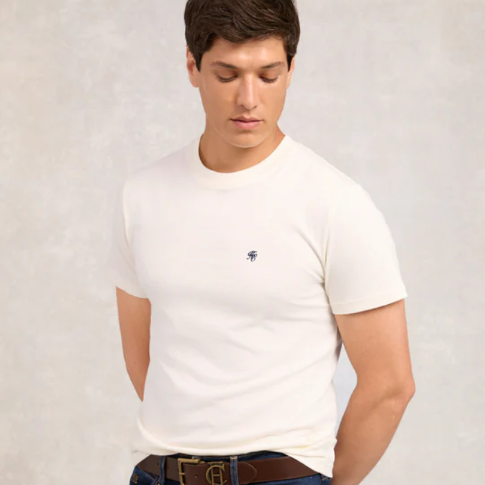 Man wearing a white t-shirt with a small logo on a plain background