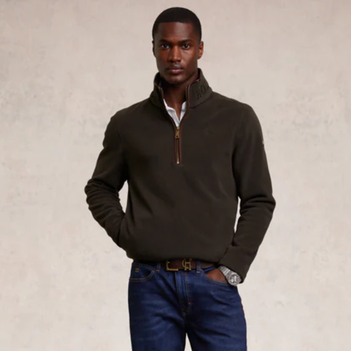 Man wearing a dark khaki half-zip sweater and blue jeans against a beige background