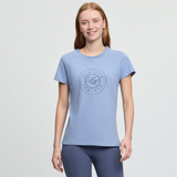 Woman wearing a light blue t-shirt with a logo on a plain background