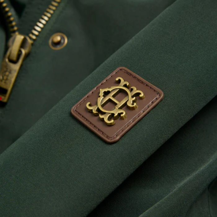 HC logo detail on brown leather square against dark green fabric
