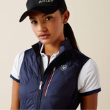 Woman wearing a navy gilet, white shirt, and black cap with 'Ariat' branding on a beige background