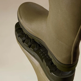 Close-up of a green wellington boot stepping onto a mirrored surface 