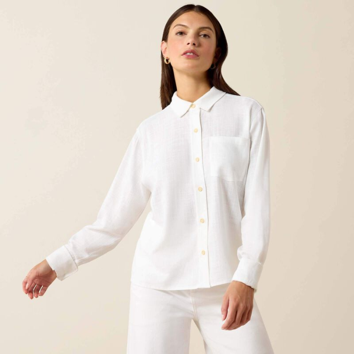 Woman wears a white linen shirt and jeans on a beige background