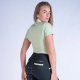 Woman wearing a light green riding shirt and black riding leggings on a white background