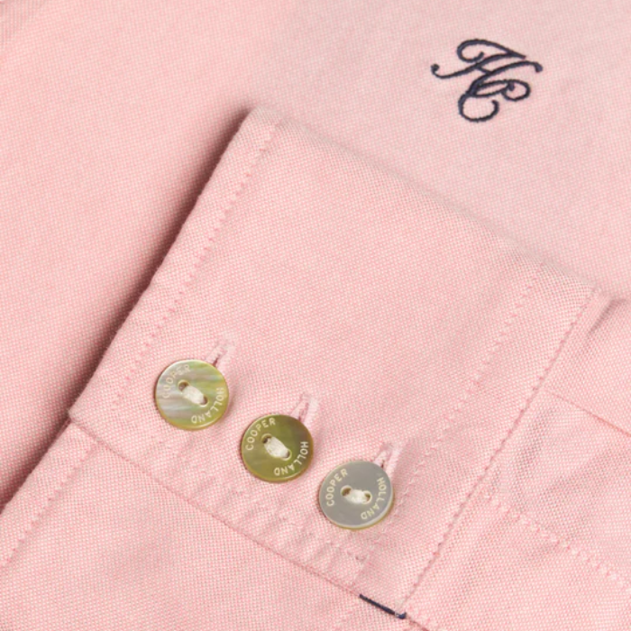 Close-up of a pink fabric with buttons and embroidered initials.