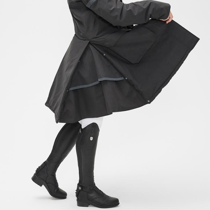 Person wears a black coat and long black riding boots against a white background