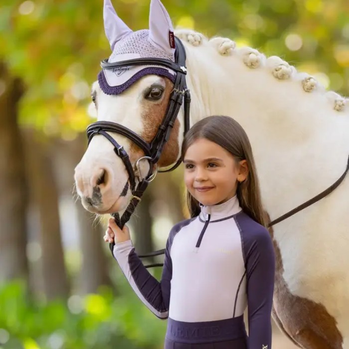 Young girl in equestrian attire standing next to a white horse with a blurred natural background