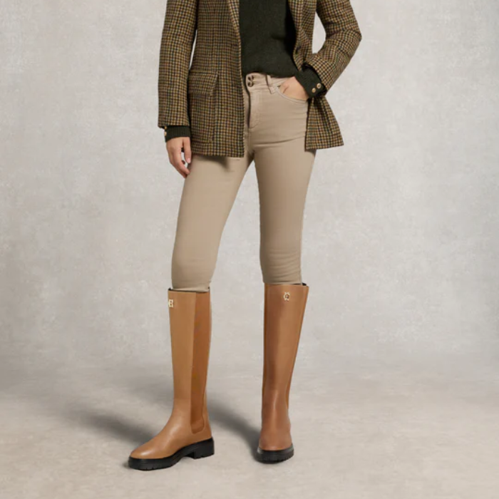 Person wearing tan knee-high boots, beige jeans, and a plaid jacket on a neutral background