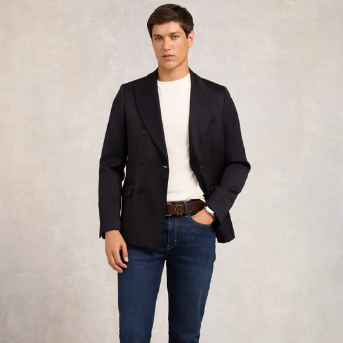 Man wearing a black blazer, white shirt, and blue jeans on a plain background