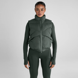 Woman wears a green gilet over an equestrian outfit on a grey background