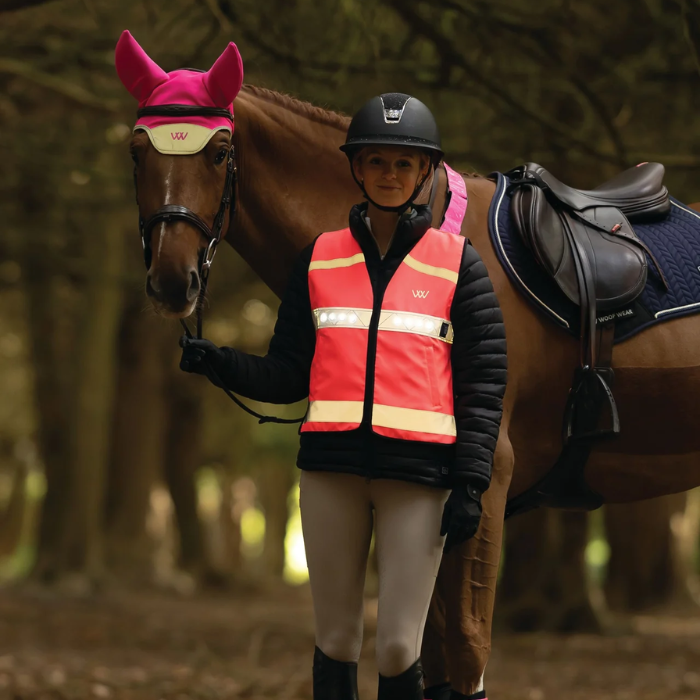 Person in equestrian gear standing next to a horse in a forest setting