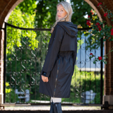 Woman wearing a black coat standing in front of a decorative archway with flowers.