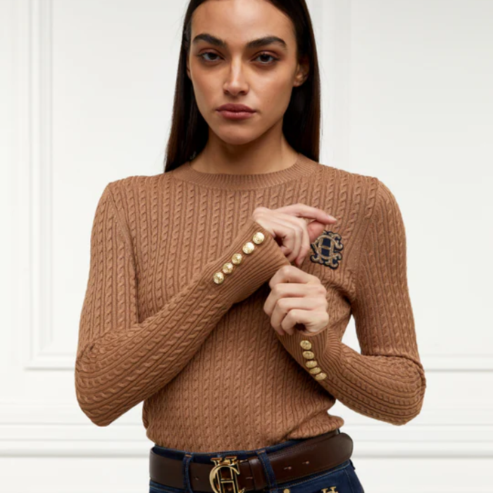 Woman wearing a brown cable knit sweater with decorative buttons against a white background