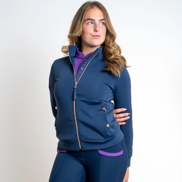 Woman wears a blue top with rose gold zip detail on a grey background