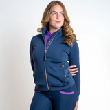 Woman wears a blue top with rose gold zip detail on a grey background